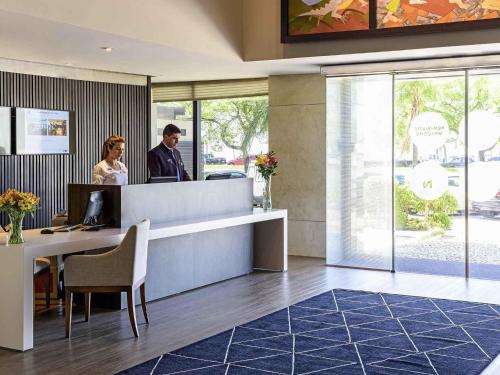 a man and a woman standing at a desk in a lobby at Novotel Florianopolis in Florianópolis