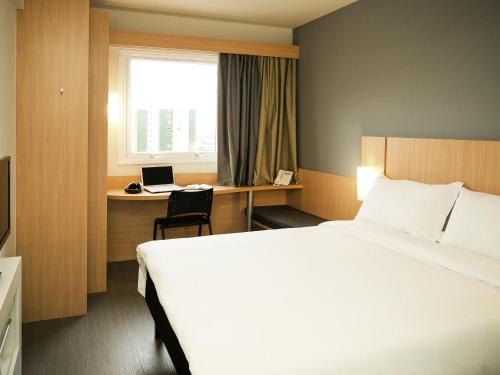 a hotel room with a bed and a desk with a laptop at ibis Cascavel in Cascavel