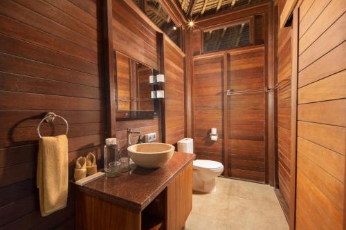 a bathroom with a sink and a toilet and wooden walls at Gecko Villa & Bungalows in Nusa Lembongan