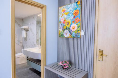 a bathroom with a painting on the wall and a bench with flowers at Cannes Ben Tre Hotel in Ben Tre