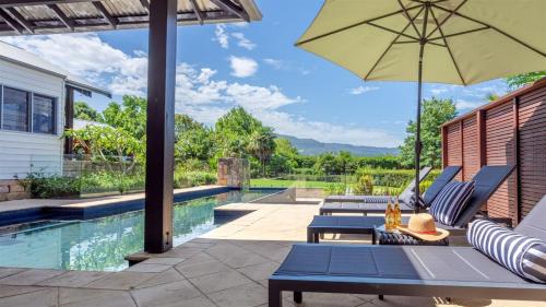 a patio with chairs and an umbrella next to a swimming pool at Fletchers Lane Escape in Meroo