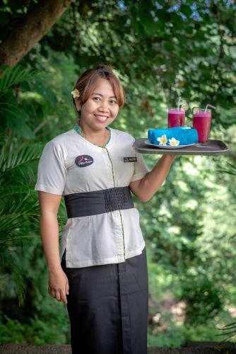a woman holding a tray with a cake and drinks at Villa Bayu - exclusive villa with infinity pool, wellness pavilion, panoramic ocean view & full service in Temukus