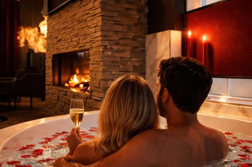 a couple sitting in a bath tub with a glass of wine at Wellness Tuin - Boudoir Suite - Ultieme Partner Beleving - Indoor Jacuzzi en Openhaard en privé Sauna - in Romantische stijl - Gratis Fles Prosecco & Leuke Partner connect box ! in Horst