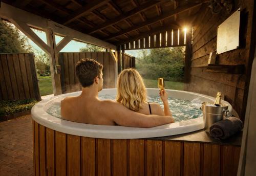 a man and a woman sitting in a bath tub at Wellness Tuin - Ultieme Partner Beleving - St Hubertus Suite met Indoor Jacuzzi, Openhaard, Privé Hottub en Privé Sauna in Jachthut stijl - Gratis Fles Prosecco & Leuke Partner connect box ! in Horst
