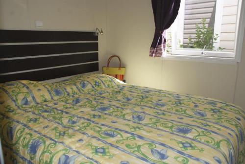 a bed with a colorful comforter in a bedroom at Camping Tikayan Clau Mar Jo - Maeva in Bormes-les-Mimosas
