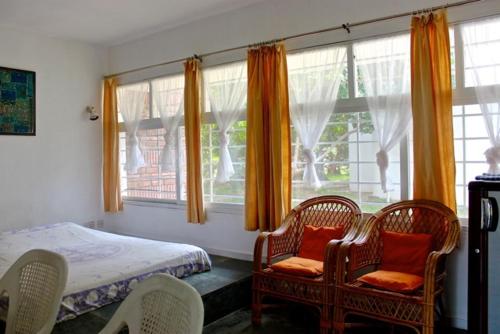 a bedroom with two chairs and a bed and windows at New Creation Guest House in Auroville