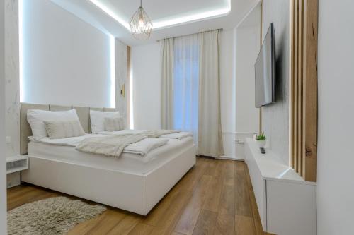 a white bedroom with a large white bed and a television at Mona Luxury Apartments - Free Garage Parking in Sarajevo