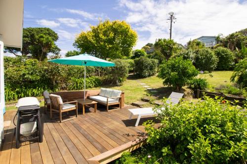 a wooden deck with a table and an umbrella at Classic bach near the beach in Oneroa