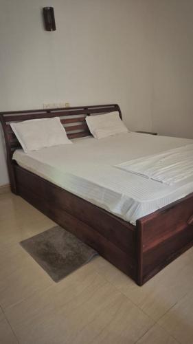 a large wooden bed with white sheets on it at Pearl City Resort in Tissamaharama