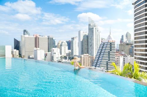 a woman sitting on the edge of a swimming pool overlooking a city at Shama Sukhumvit Bangkok in Bangkok