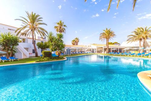 a large swimming pool with palm trees and buildings at Vibra Blanc Cottage Apartmentos - 3SUP in Sa Caleta
