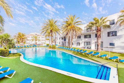 an outdoor swimming pool with blue chairs and palm trees at Vibra Blanc Cottage Apartmentos - 3SUP in Sa Caleta