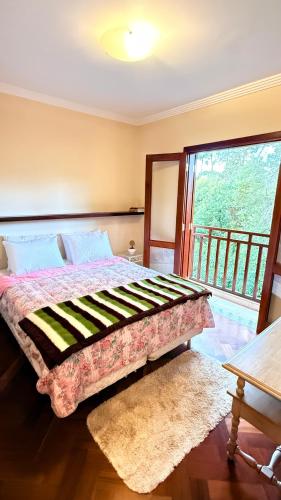 a bedroom with a bed and a large window at Espaçoso Apto triplo a 300 mts do Centrinho Capivari in Campos do Jordão