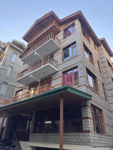 a tall brick building with a balcony on it at Hotel The Red Apple in Manāli