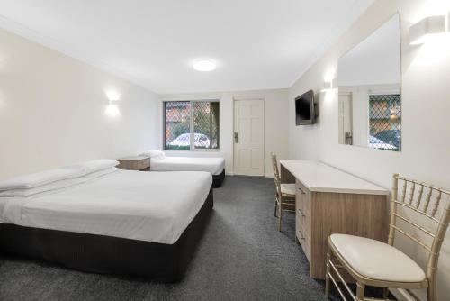 a hotel room with two beds and a desk at Elizabethan Lodge in Melbourne