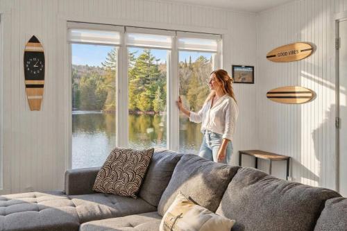 a woman standing in a living room looking out a window at Bécassines Private Spa & Pool table , Waterfront in Nominingue