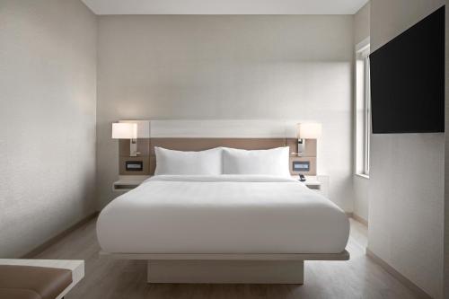 a bedroom with a large white bed and a television at AC Hotel by Marriott Gainesville Downtown in Gainesville