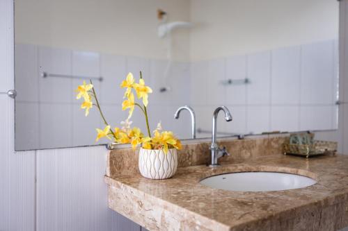 a bathroom counter with a sink with yellow flowers in a vase at Hotel SPA Paraíso in Cruzeiro do Sul