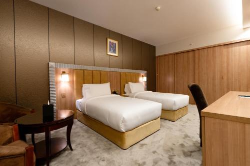 a hotel room with two beds and a desk at Luxe Grand Hotel in Dubai
