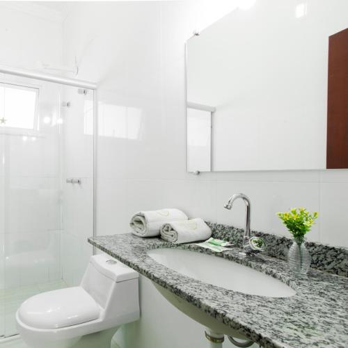 a white bathroom with a sink and a toilet at Hotel Stelati in Jaguariúna
