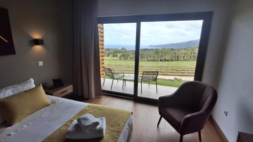 a bedroom with a bed and a chair and a large window at Refúgio dos Capelinhos - Villa e Suites in Norte Pequeno