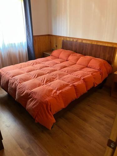 a bed with an orange comforter in a bedroom at Cabañas arca 2 in Pucón