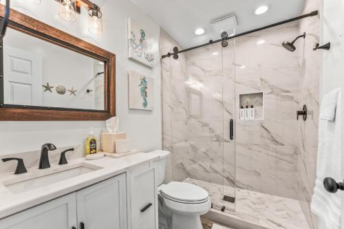 a white bathroom with a shower and a toilet at Oceanfront St Helena Island Condo w/ Beach Access! in Oceanmarsh Subdivision