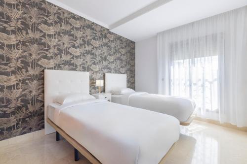 two beds in a room with a wall with floral wallpaper at BHost - Bellagio II in Benalmádena