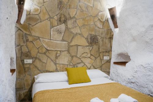a bed in a room with a stone wall at Cuevas El Atochal Orígenes in Gor