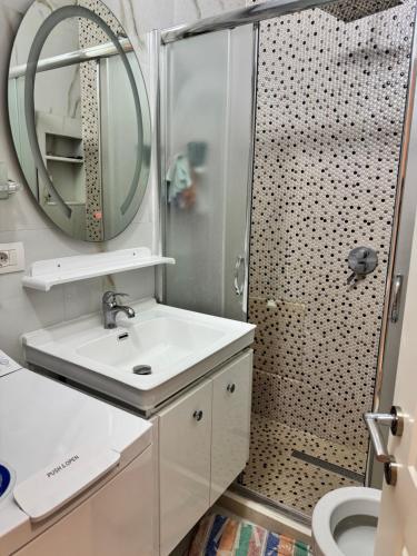 a bathroom with a sink and a shower with a mirror at Arli's SeaFront Apartaments in Durrës