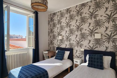 a bedroom with two beds and a wall with palm wallpaper at Hôtel Parc Mazon-Biarritz in Biarritz