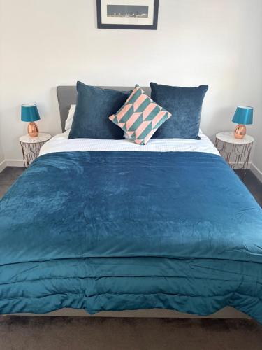 a bed with a blue comforter and two lamps at 1 Shiphouse Apartment in Lamlash