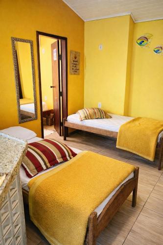a yellow room with two beds and a mirror at Pousada Casarão Piúma in Piúma