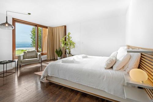 a white bedroom with a large bed and a chair at Studio with panoramic view in Bellerive