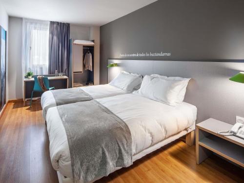 a bedroom with a large white bed and a desk at ibis Styles Pamplona Noain in Noáin