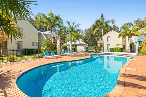 a swimming pool with blue chairs and palm trees at Bec's Beach House Getaway in Batemans Bay