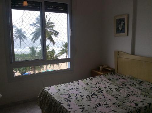 a bedroom with a bed and a window with a palm tree at Pitangueiras Frente Total Mar pé na areia in Guarujá