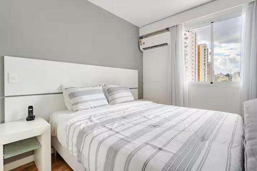 a white bedroom with a bed and a window at Flat Hotel Vila Olímpia in São Paulo