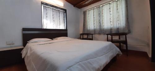 a bedroom with a white bed and two windows at Leela Villa - Ancient Redstone Escape in Panchgani