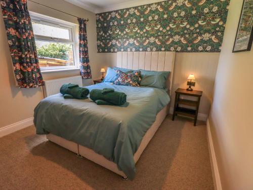 a bedroom with a bed with green sheets and a window at Yew Tree Cottage in Wigton