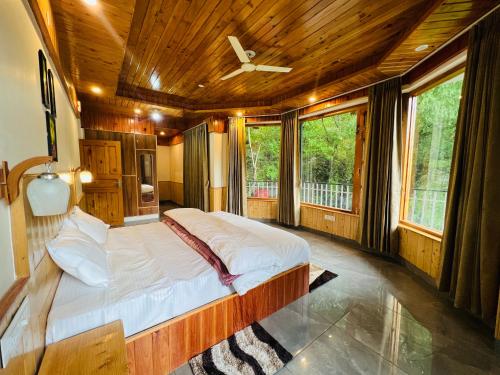 a bedroom with a large bed in a room with windows at Tirthan Villa Homestay in Banjār