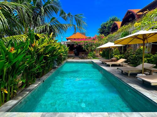 a swimming pool with chairs and umbrellas next to a house at Puri Melati in Uluwatu