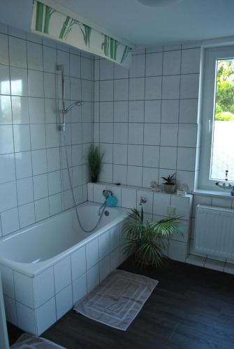 a white tiled bathroom with a tub and a plant at Ferienwohnung Thiedmann in Hagebök