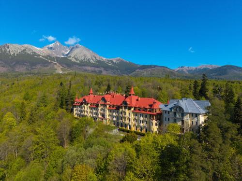 a large building on a hill with mountains in the background at Grand Hotel Praha in Tatranská Lomnica