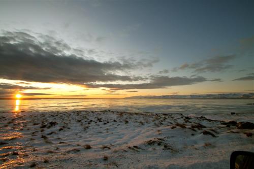 a sunset on a beach with the ocean at Hvammur Apartments by the Harbour in Höfn