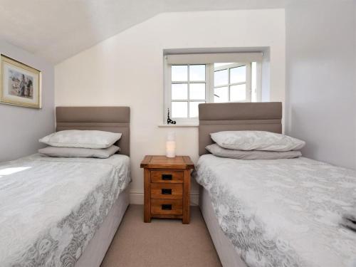 two beds in a room with a night stand and a window at 2 Bed in Crediton oc-51275 in Stockleigh Pomeroy