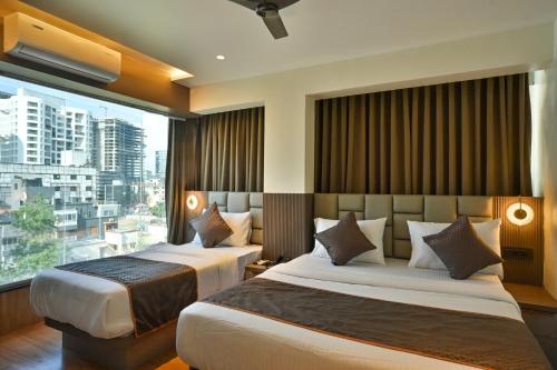 two beds in a hotel room with a large window at Hotel Emersion Residency in Pune
