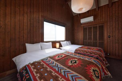two beds in a room with wooden walls and a window at IZA moriyama in Moriyama