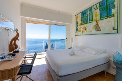 a bedroom with a bed and a desk and a large window at Villa Eze Vue Mer in Éze
