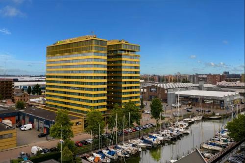 a tall yellow building next to a marina with boats at Holiday Inn Express Amsterdam - North Riverside by IHG in Amsterdam